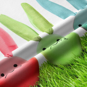 Zbliżenie na fakturę tkaniny i detal pasujących pastelowych jajek z uszami z nadrukiem zajączków na trawie