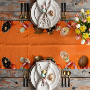 aranżacja stołu z bieżnikiem: talerze, sztućce i bukiet wiosennych kwiatów na pomarańczowym tle