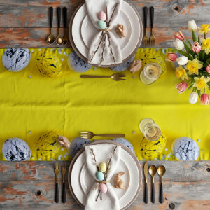 Aranżacja stołu z bieżnikiem, zastawą, bukietem tulipanów i dekoracyjnymi pisankami