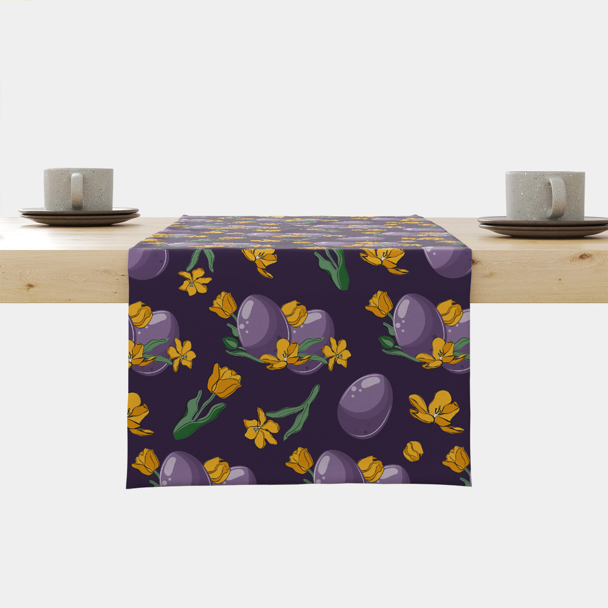 Bieżnik na stole z motywem fioletowych pisanek i żółtych tulipanów ułożony na drewnianym stole z filiżankami