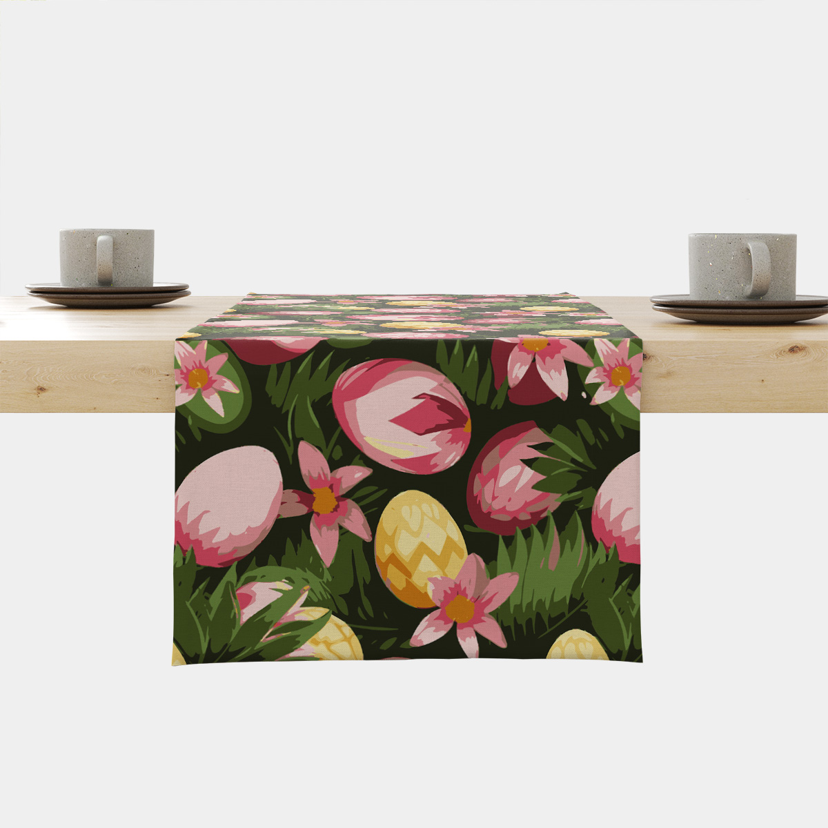 Bieżnik z motywem różowych i żółtych pisanek oraz kwiatów na ciemnozielonym tle, widok z przodu na stole z filiżankami