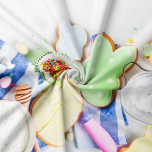 Zbliżenie na pastelowe ciasteczka w kształcie jajek i zajączków oraz drobne posypki na tle faktury tkaniny