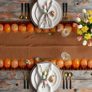 Aranżacja stołu z bieżnikiem, zastawą, tulipanami i rzędem pomarańczowych pisanek przy nakryciach