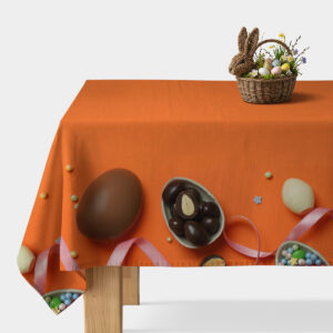 stół nakryty pomarańczowym obrusem z motywem czekoladowych jajek, miseczek ze słodyczami i różową wstążką