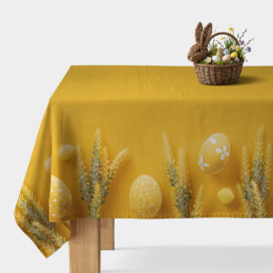 żółty obrus z motywem pisanek i kłosów na stole z koszykiem wielkanocnych dekoracji