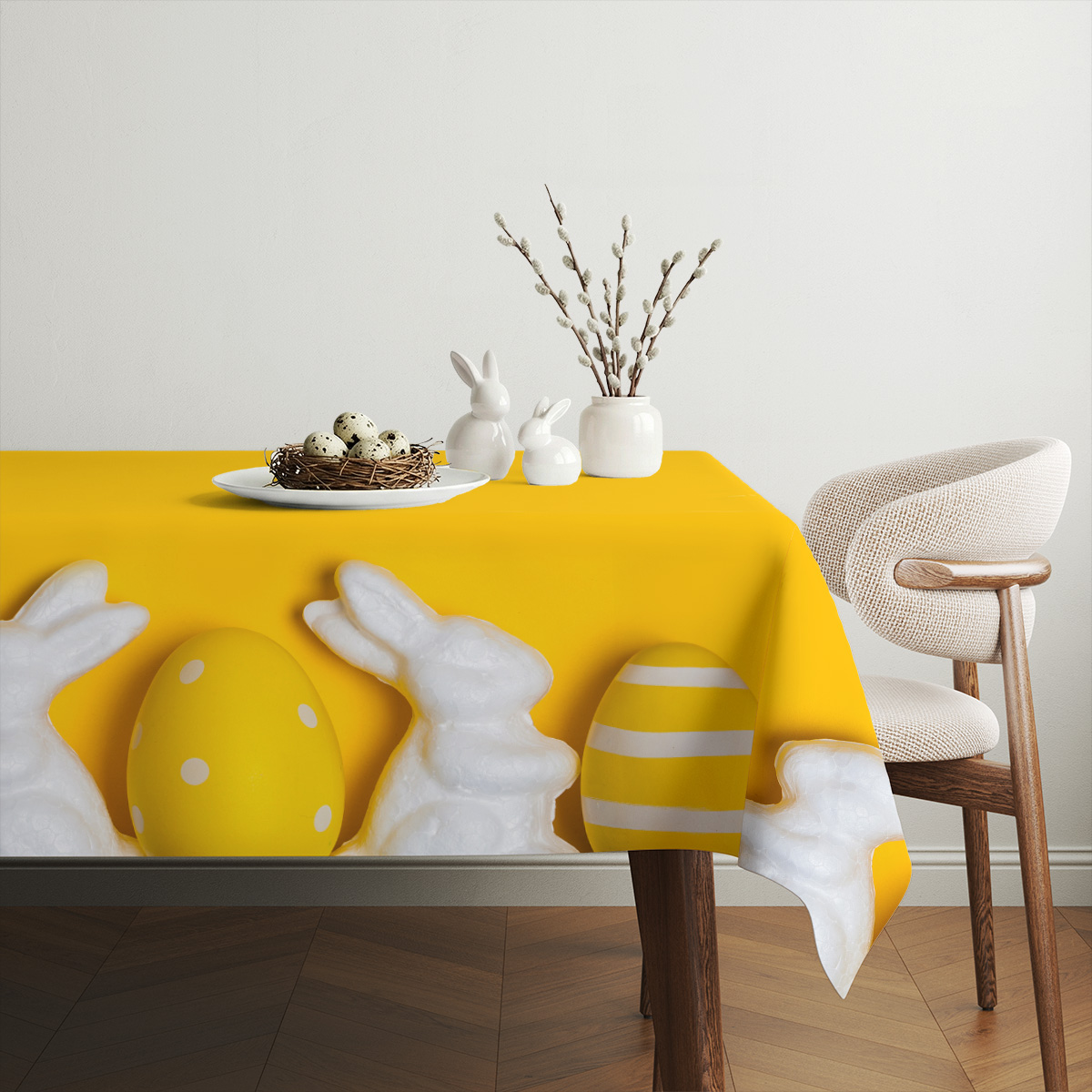 Aranżacja stołu z gniazdem jajek, ceramicznymi zajączkami i gałązkami bazi na żółtym obrusie