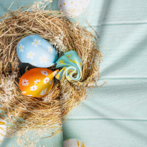 zbliżenie na gniazdo ze słomą i pastelowymi pisankami na tle miętowego materiału