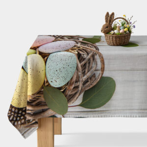 Stół nakryty obrusem z motywem pastelowych pisanek w wiklinowym gnieździe — ujęcie główne