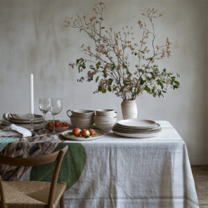 Widok na nakryty stół z obrusem i dekoracyjnymi gałązkami w neutralnym wnętrzu