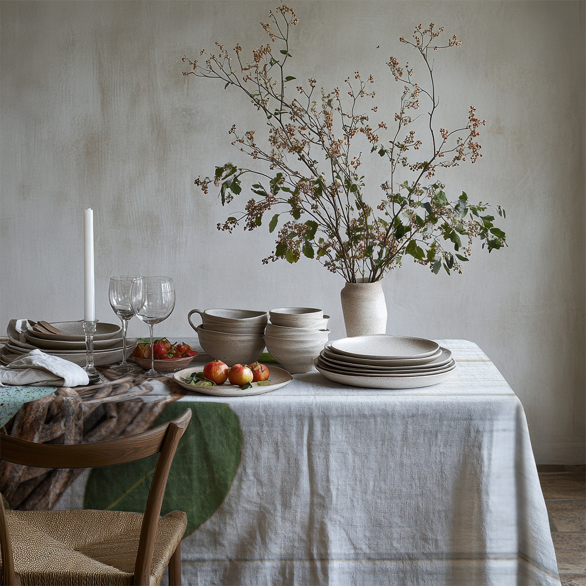 Widok na nakryty stół z obrusem i dekoracyjnymi gałązkami w neutralnym wnętrzu