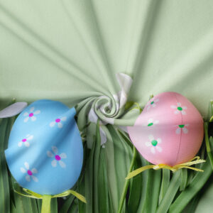 Zbliżenie na pastelowe jajka i drobne białe kwiatki na materiale obrusowym