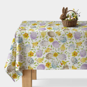 stół nakryty obrusem w akwarelowe pisanki i kurczaczki z wiklinowym koszykiem na jajka