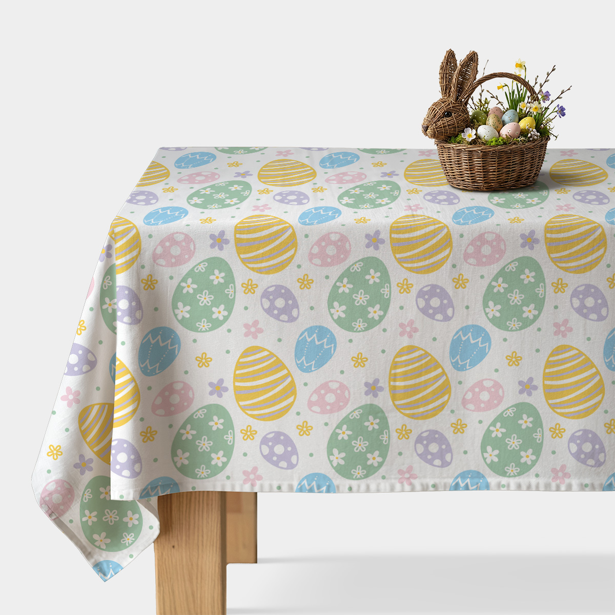 Obrus z motywem pastelowych pisanek i drobnych kwiatków na jasnym tle z koszykiem wielkanocnym