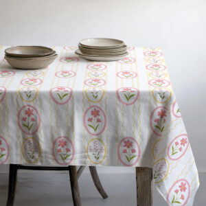 Stół nakryty obrusem z wzorem pisanek z ułożonymi ceramicznymi talerzami i miseczkami