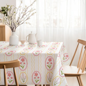 Jasna jadalnia z obrusie w pastelowe medaliony, wazon z kwiatami i drewniane krzesła