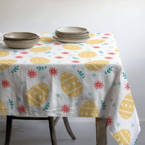 Stół zastawiony miskami i talerzami na obrusie z żółtymi pisankami i zielonymi listkami
