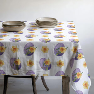 Obrus z powtarzalnym wzorem pisanek i żonkili pod zastawą talerzy i miseczek