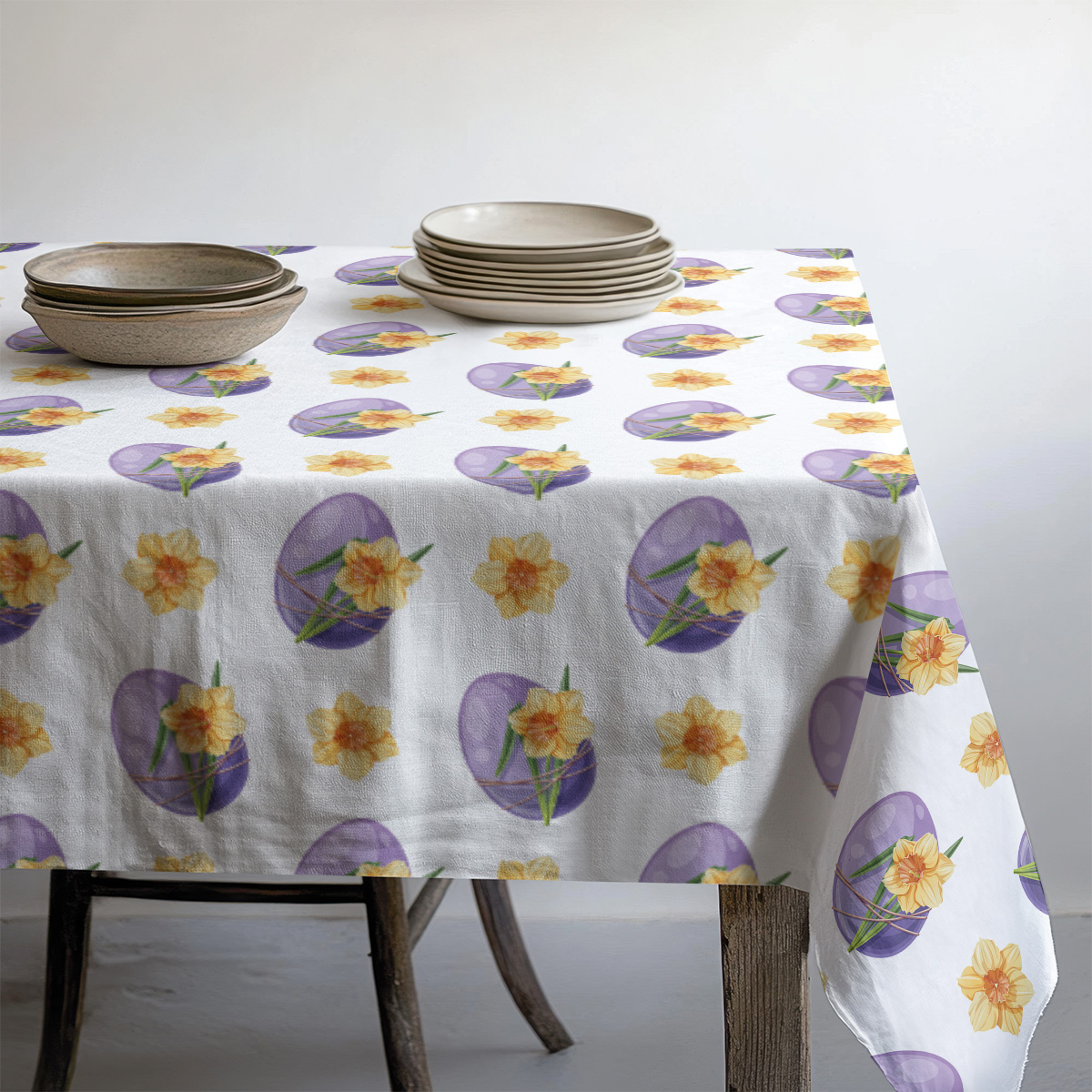 Obrus z powtarzalnym wzorem pisanek i żonkili pod zastawą talerzy i miseczek