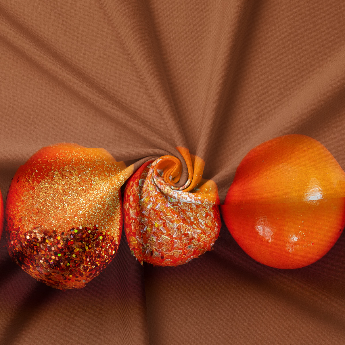 zbliżenie na ozdobne pomarańczowe pisanki z połyskiem i brokatową fakturą na materiale