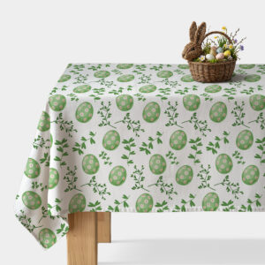 Obrus z motywem zielonych pisanek i zielonych gałązek na białym tle, widok na nakryty stół z koszykiem wielkanocnym