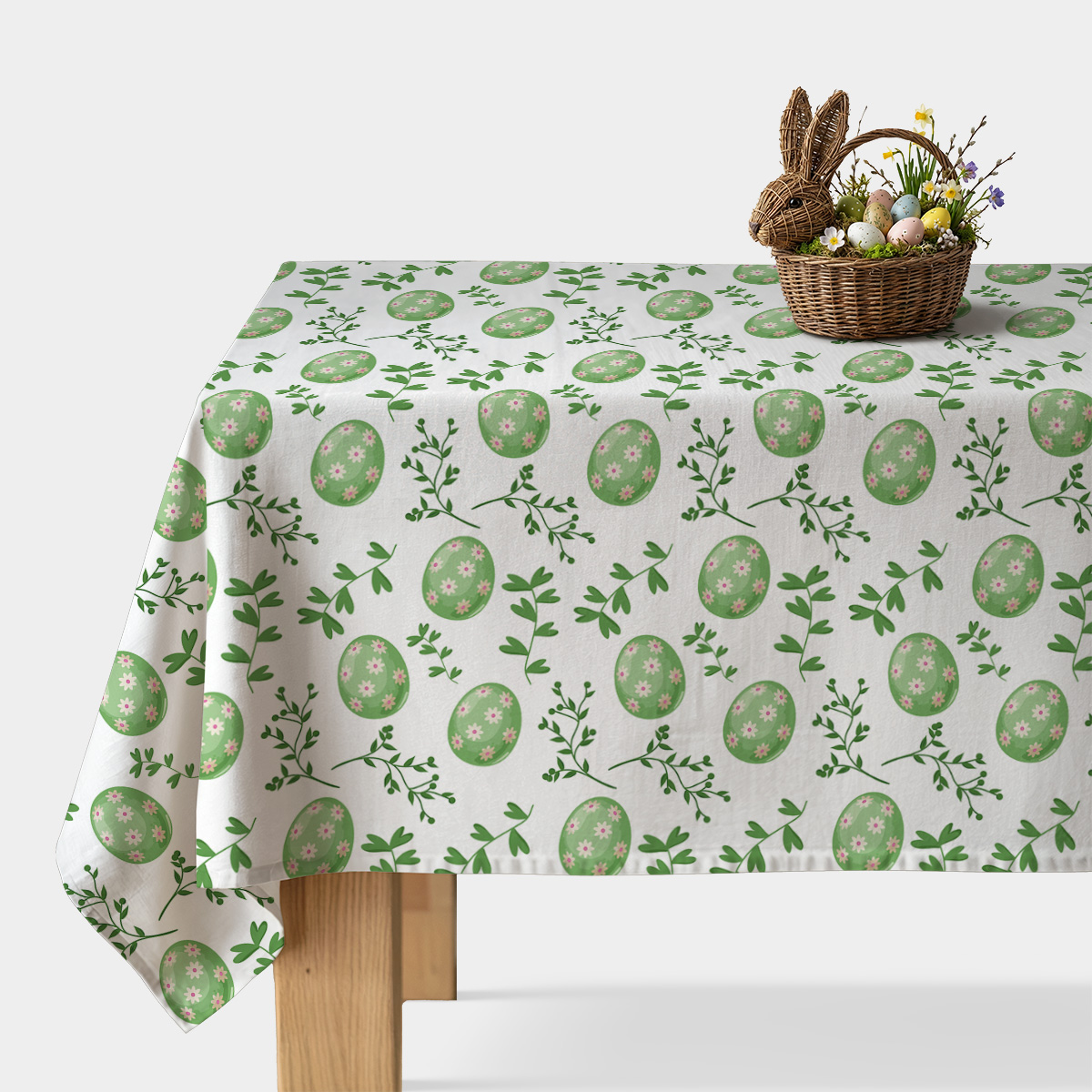 Obrus z motywem zielonych pisanek i zielonych gałązek na białym tle, widok na nakryty stół z koszykiem wielkanocnym