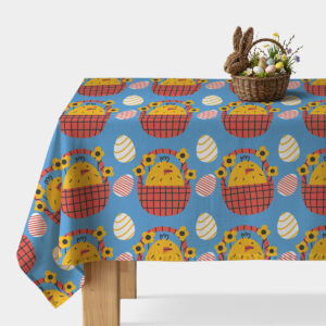 Stół przykryty obrusem z wielkanocnym wzorem kurczaczków w koszykach oraz koszyk dekoracyjny z pisankami