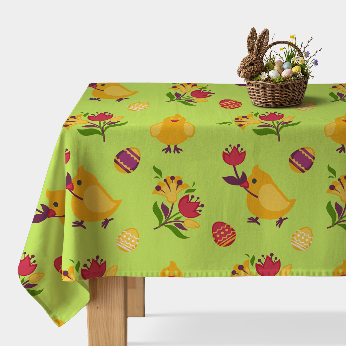 Główny widok obrusu na stole z wiosennym wzorem kurczaczków, pisanek i kwiatów oraz koszykiem z dekoracjami