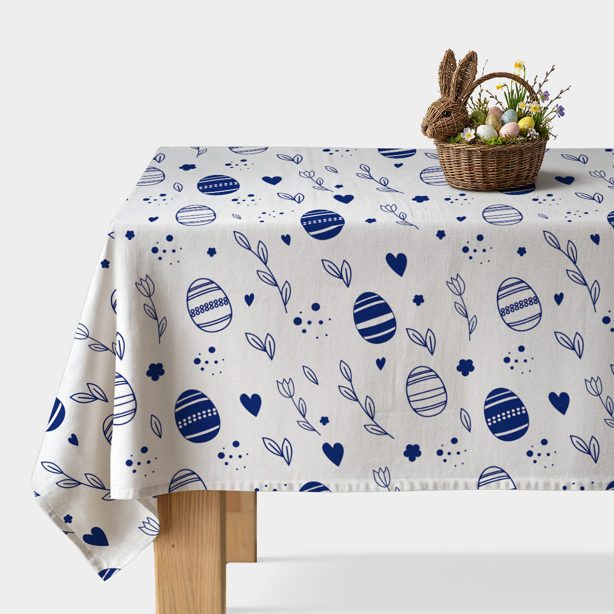 biały obrus z granatowymi pisankami, gałązkami i serduszkami na stole z koszykiem wielkanocnym