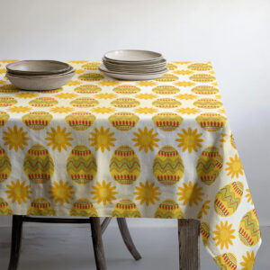 Stół nakryty obrusem z motywem pisanek z ułożonymi naczyniami i talerzami