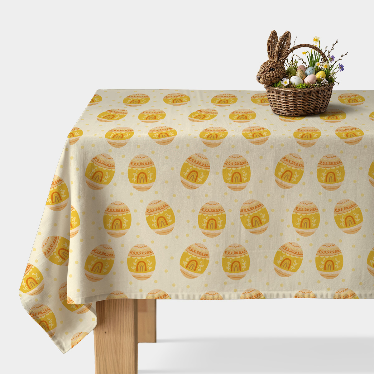Obrus z wzorem żółtych pisanek na kremowym tle na stole z koszykiem wielkanocnym