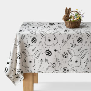 Stół nakryty obrusem z motywem króliczków i pisanek, na rogu koszyk z wielkanocnymi jajkami