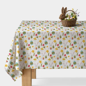 stół nakryty obrusem z wiosennym wzorem z zajączkami, pisankami i kwiatami z koszykiem wielkanocnym
