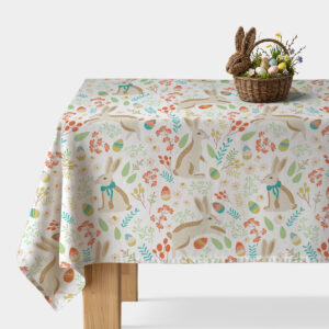 Obrus z wielkanocnym wzorem z zajączkami i pisankami ułożony na stole z wiklinowym koszykiem z jajkami