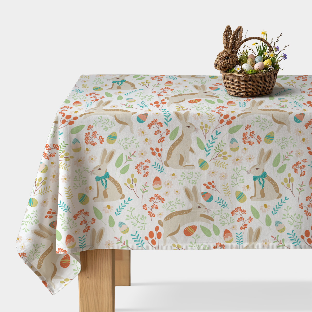 Obrus z wielkanocnym wzorem z zajączkami i pisankami ułożony na stole z wiklinowym koszykiem z jajkami