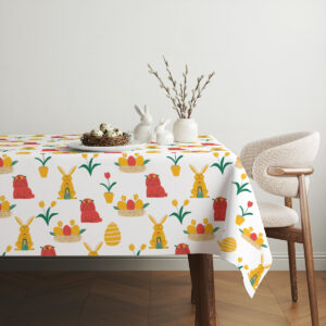 Aranżacja stołu z obrusem w wielkanocne motywy, dekoracje z białych gałązek i ceramiczne zajączki