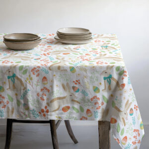 Detal narożnika stołu pokazujący pastelowy wzór zajączków, pisanek i liści na brzegu obrusu
