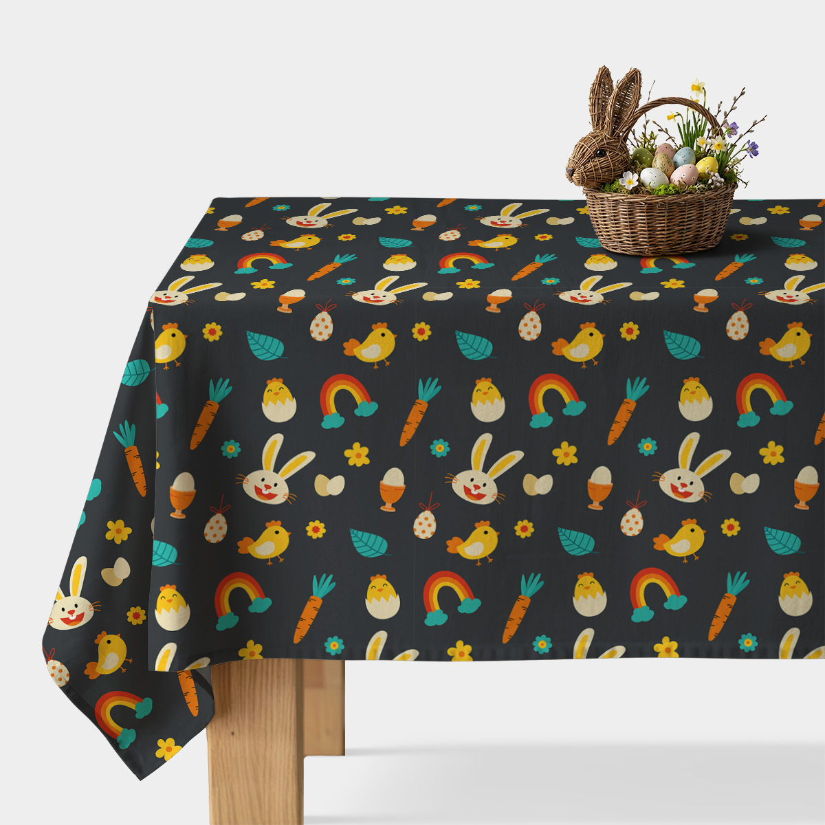 Obrus z ciemnym tłem ozdobiony kolorowymi wielkanocnymi motywami na stole z wiklinowym koszykiem z pisankami