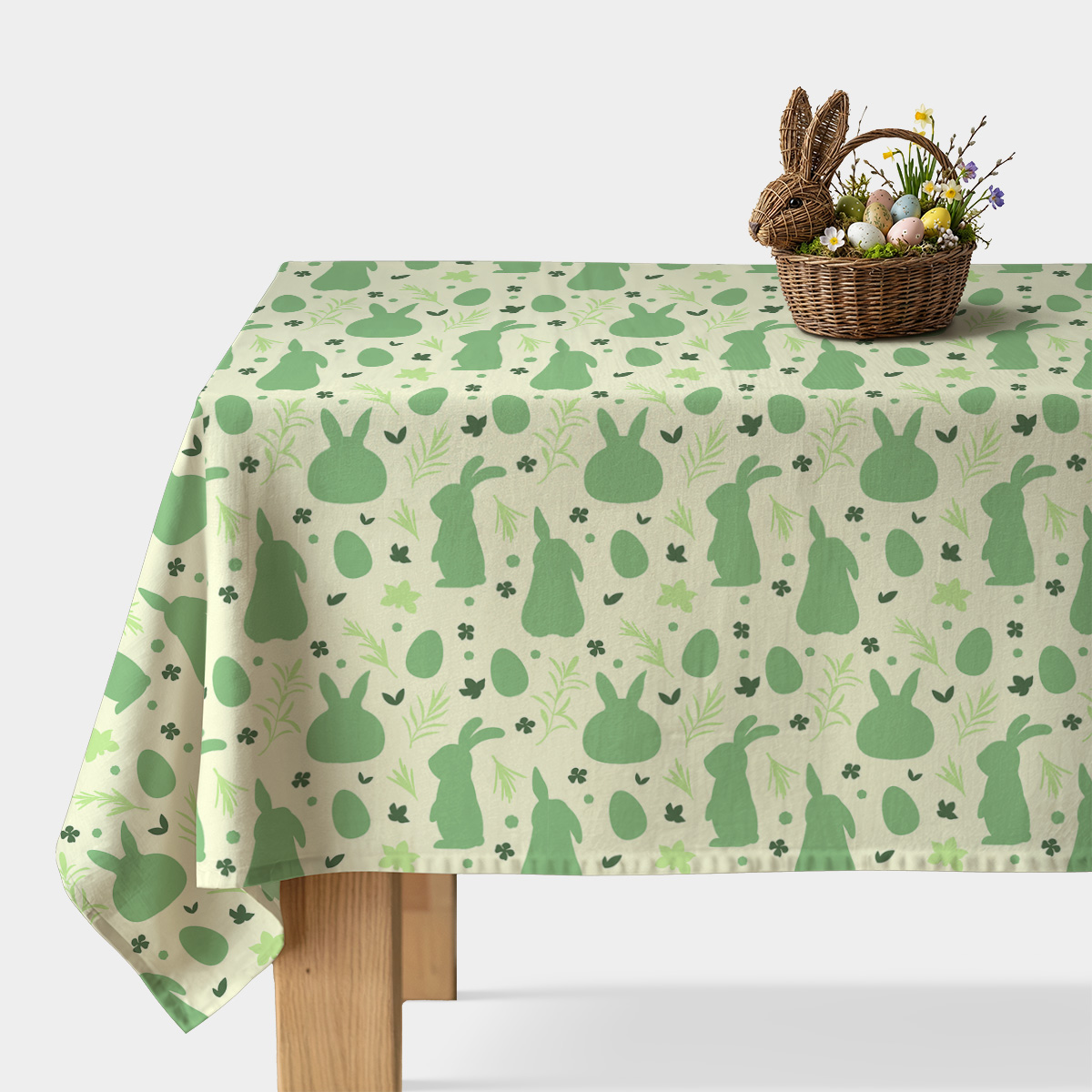 Obrus z motywem zielonych zajączków i pisanek na stole z wiklinowym koszykiem z jajkami