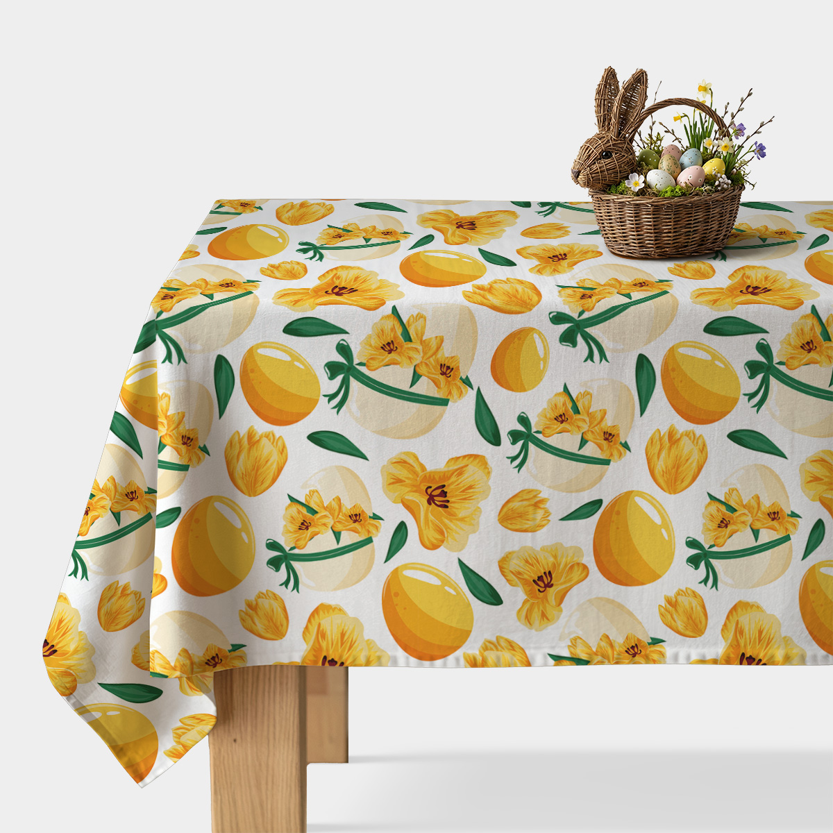 główne ujęcie stołu z obrusem w żółte pisanki i wiosenne kwiaty oraz wiklinowym koszykiem z dekoracyjnymi jajkami