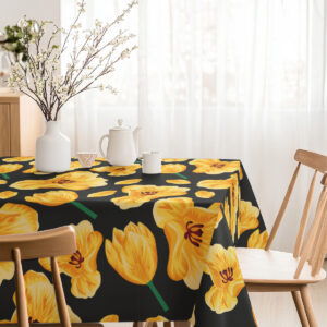 Ujęcie całego blatu z obrusem w żółte tulipany ozdobionego wazonem z gałązkami i naczyniami