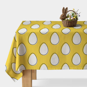 Obrus na żółtym tle z powtarzalnymi białymi pisankami, główne ujęcie stołu z koszykiem wielkanocnym