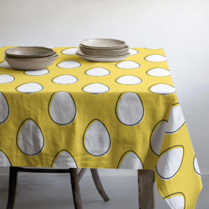 Ujęcie stołu z talerzami i naczyniami, które eksponuje wzór białych pisanek na żółtym tle