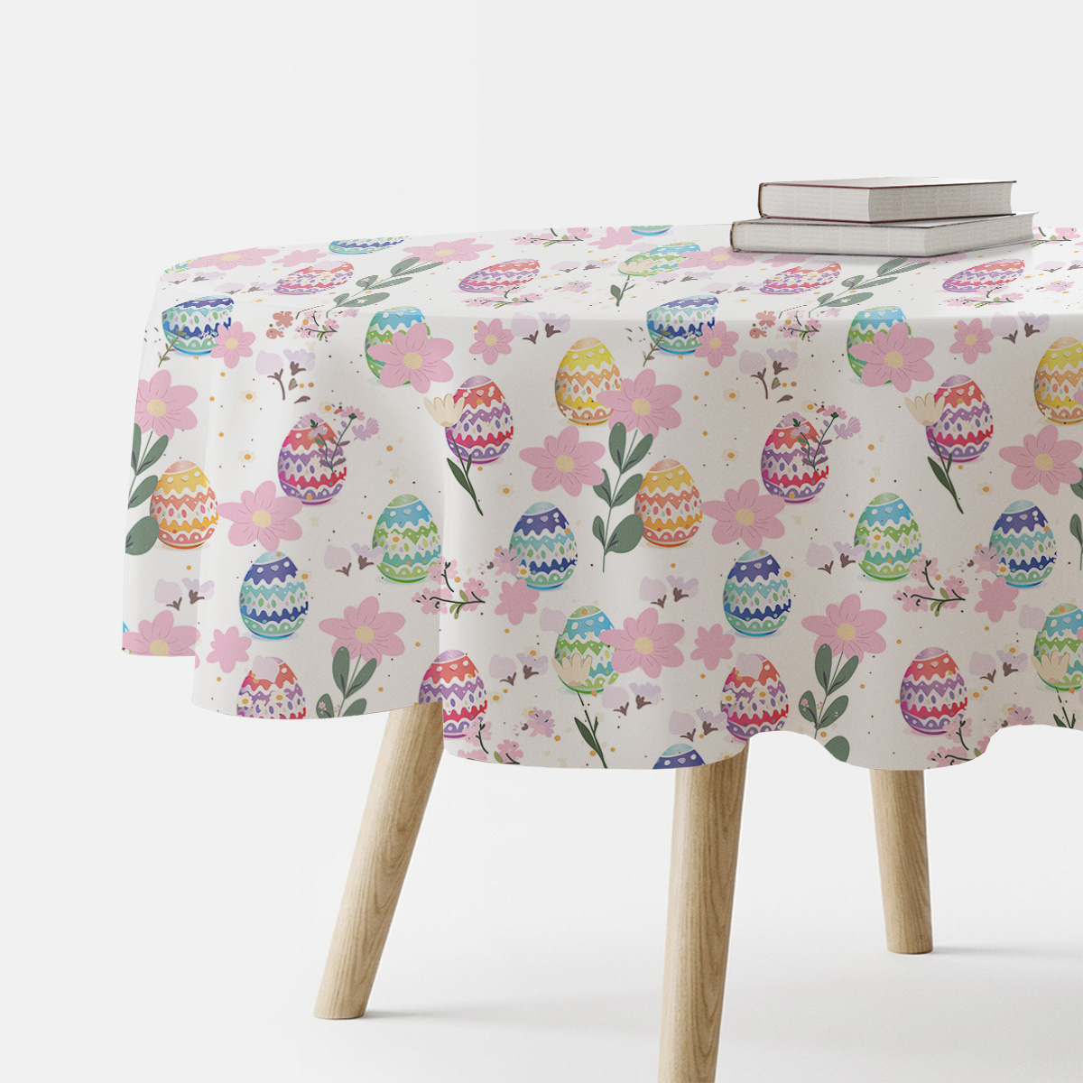 Okrągły obrus z motywem pastelowych pisanek i różowych kwiatów na stole, widok z boku z książkami jako aranżacja