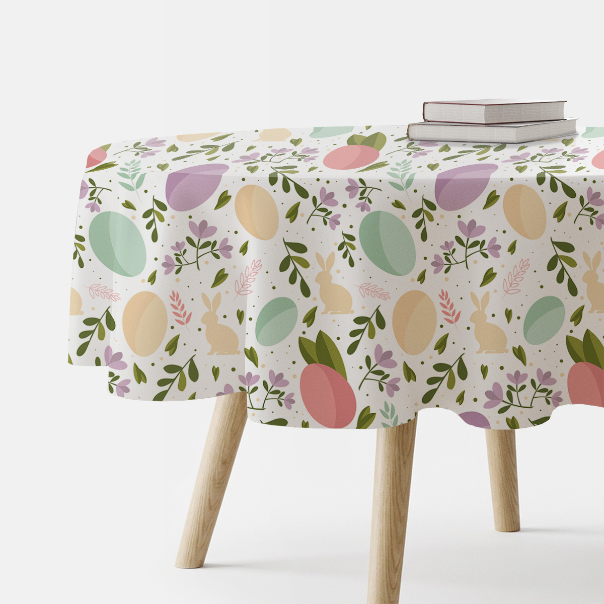 Okrągły obrus z wzorem pastelowych pisanek i zajączków na stole, widok z boku z kawałkiem książek na stole