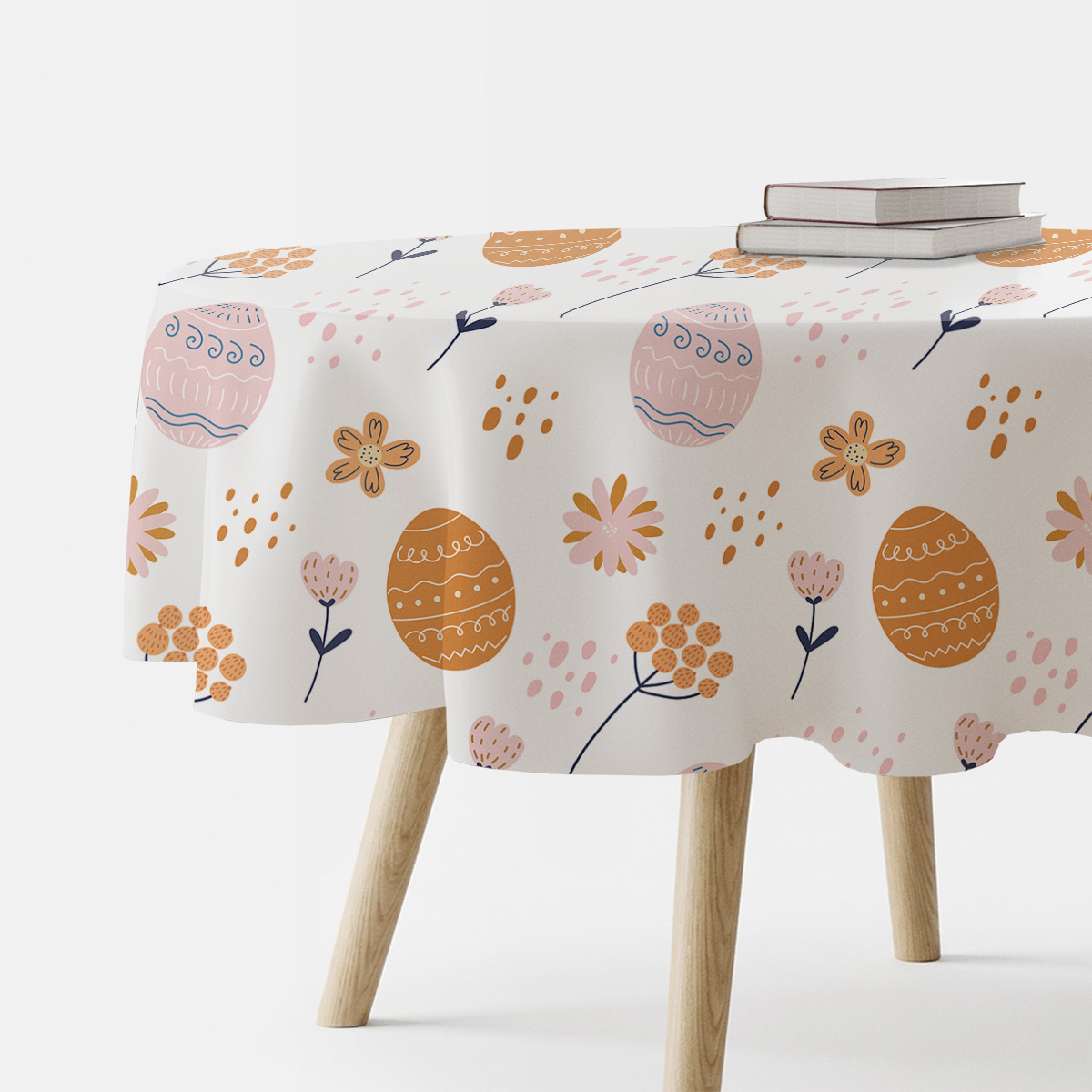 Okrągły obrus z motywem pisanek i delikatnych kwiatów na białym tle, aranżacja z książkami na stole