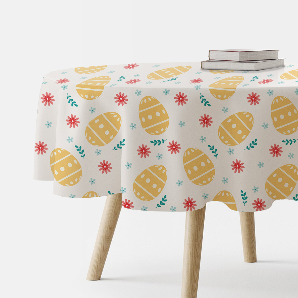 okrągły obrus z motywem żółtych pisanek i wiosennych kwiatów na jasnym tle, aranżacja z książkami na stole