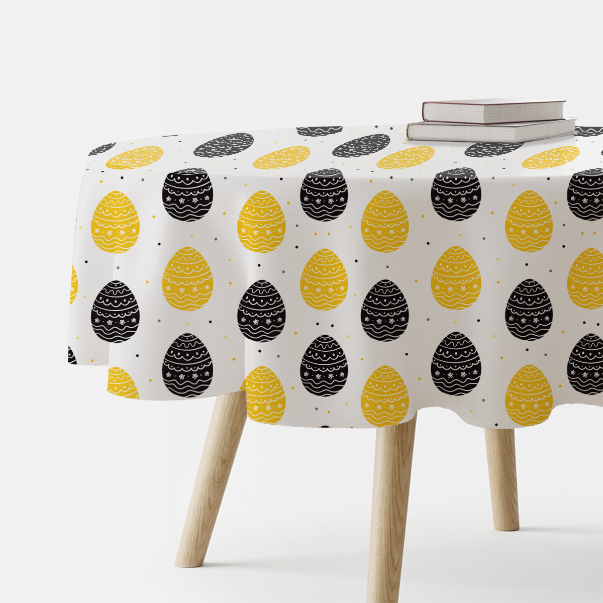 Okrągły obrus z wzorem żółtych i czarnych pisanek na białym tle, ujęcie z boku na stół z książkami