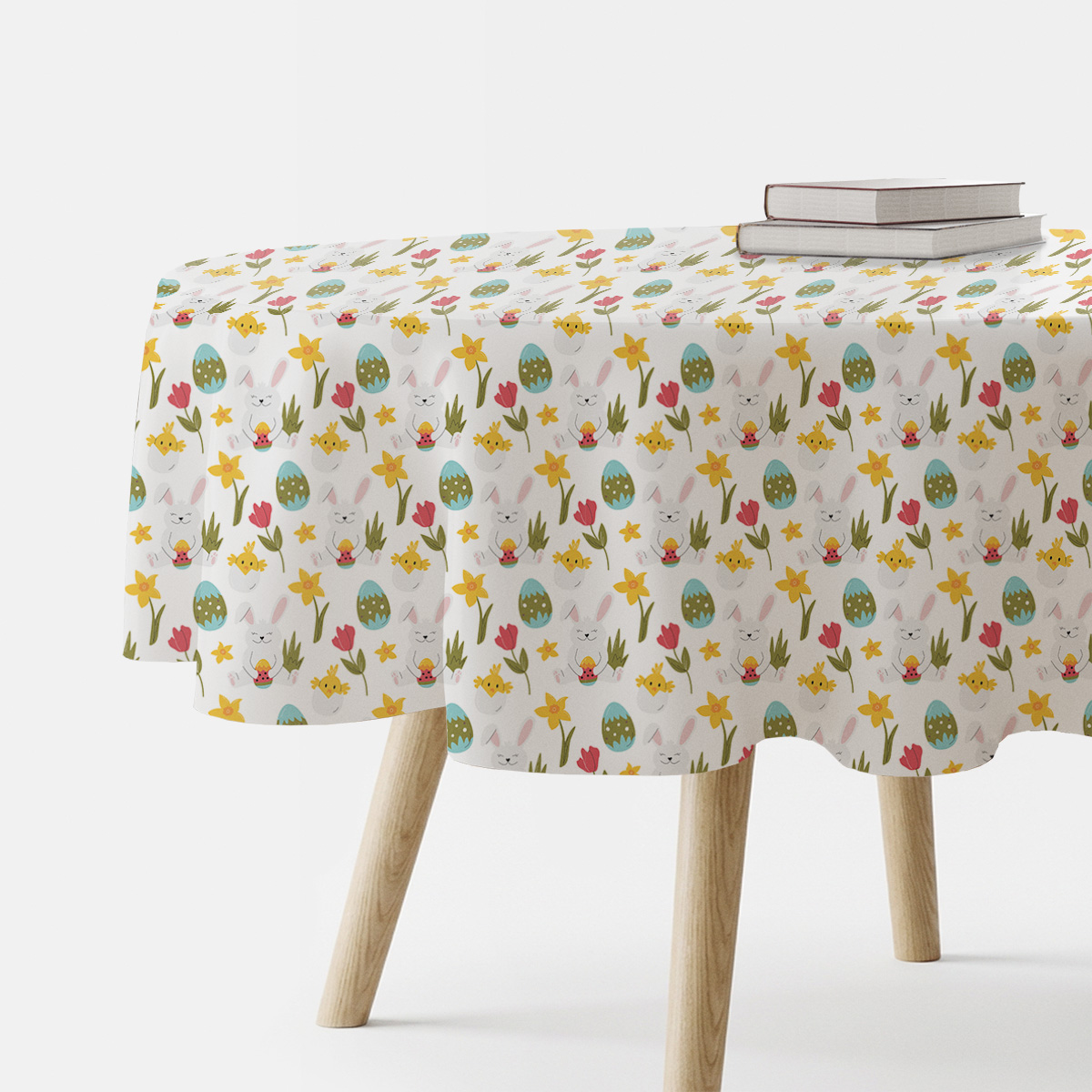 Okrągły obrus z motywem wielkanocnych zajączków i pisanek na białym tle, ujęcie stołu z boku z książkami na blacie