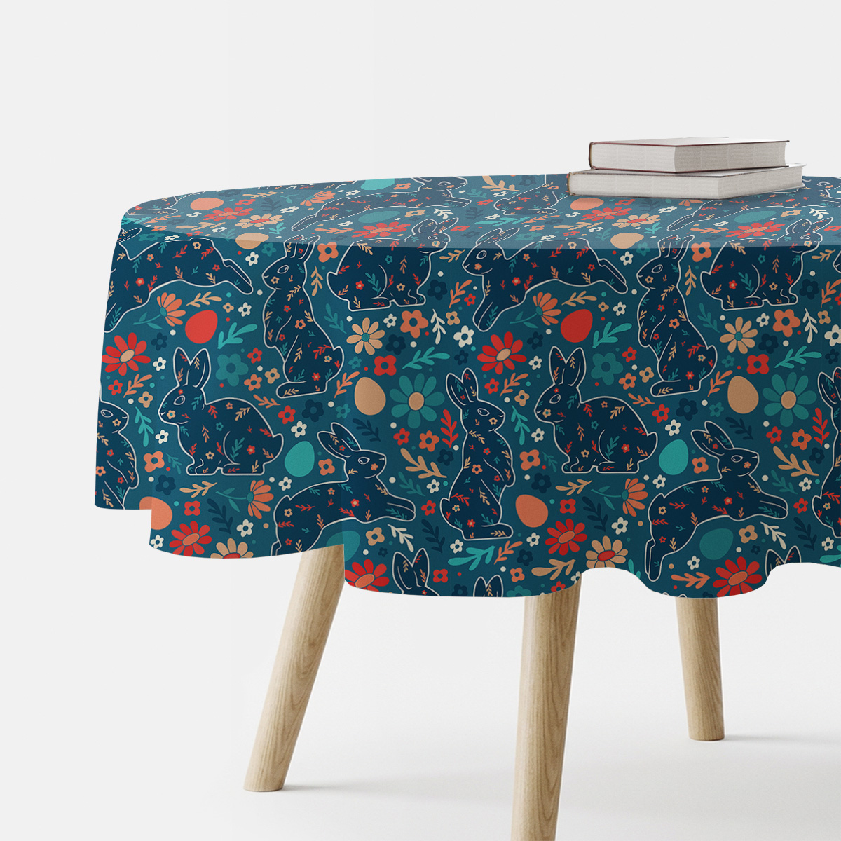 Okrągły obrus z wzorem zajączków i kwiatów na granatowym tle, widok fragmentu stołu z książkami