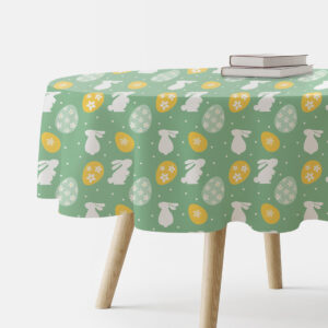 Okrągły obrus z motywem białych zajączków i żółtych pisanek na zielonym tle rozłożony na drewnianym stole